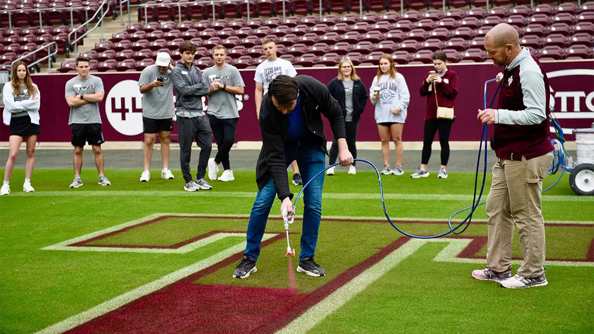 people watching a man spray the paint on the football field